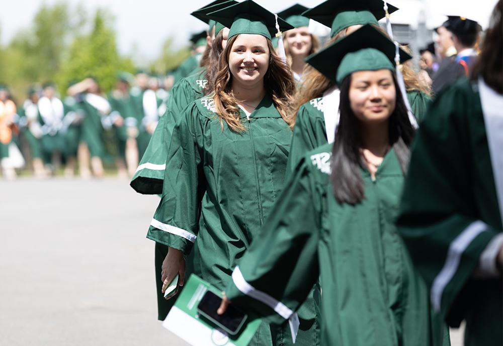 Female students being hooded by college president Joanie Mahoney (left) and male professor (right).